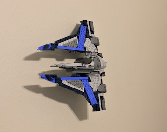 May include: A blue and gray Lego spaceship with a detailed design. The spaceship has a pointed nose and wings that are angled upwards.