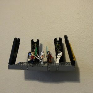Puede incluir: Un set de juego Lego Star Wars con una plataforma negra y gris con cuatro puertas negras y grises. Las puertas están abiertas y revelan una escena con cinco minifiguras Lego, incluyendo un Stormtrooper, un Jedi y un Sith.