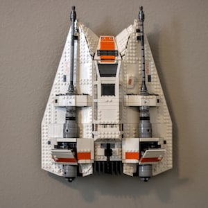 Peut inclure: Un vaisseau spatial Lego blanc et orange avec deux moteurs à l'arrière. Le vaisseau spatial est monté sur un mur.