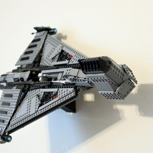 Puede incluir: Maqueta de nave espacial Lego gris y negra, montada en una pared blanca. El modelo presenta alas anguladas, paneles detallados y peque&ntilde;os detalles verdes y azules. La nave espacial es una r&eacute;plica detallada de un veh&iacute;culo de ficci&oacute;n.