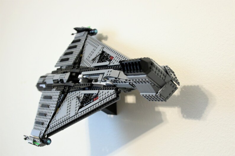 Puede incluir: Maqueta de nave espacial Lego gris y negra, montada en una pared blanca. El modelo presenta alas anguladas, paneles detallados y peque&ntilde;os detalles verdes y azules. La nave espacial es una r&eacute;plica detallada de un veh&iacute;culo de ficci&oacute;n.