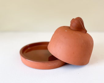 May include: Terracotta butter dish with a lid shaped like a small onion. The dish is glazed and has a smooth, shiny finish.