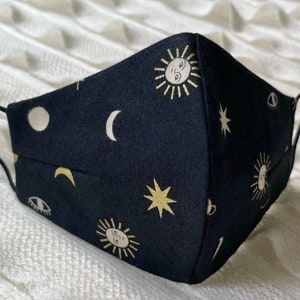 May include: Black face mask with a repeating pattern of gold suns, moons, and stars. The mask has black elastic ear loops.