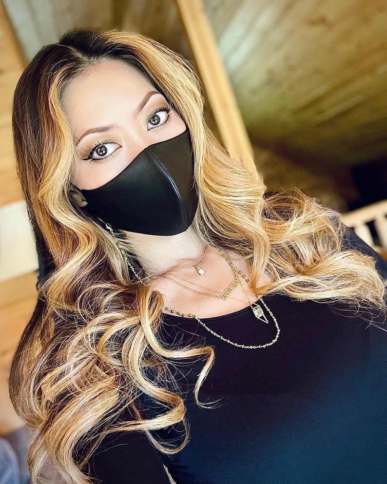 Puede incluir: Una mujer con el pelo largo y rubio lleva una mascarilla facial negra y un collar de oro de varias capas. El collar tiene un peque&ntilde;o colgante con la palabra "forever" en &eacute;l.