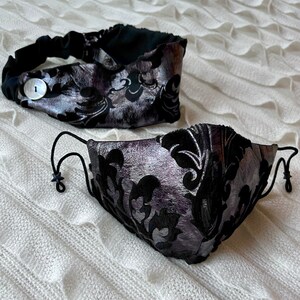 Puede incluir: Una diadema y una mascarilla negra y plateada con un patr&oacute;n floral. La diadema tiene un bot&oacute;n en el lateral.