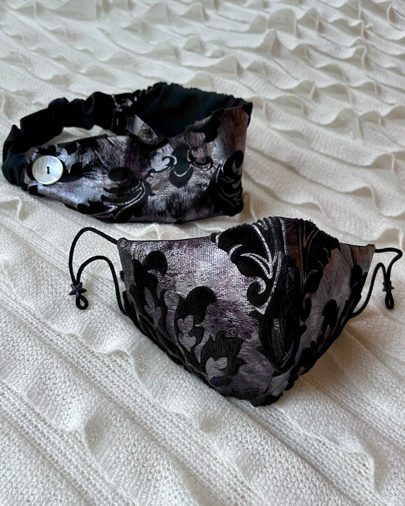 Puede incluir: Una diadema y una mascarilla negra y plateada con un patr&oacute;n floral. La diadema tiene un bot&oacute;n en el lateral.