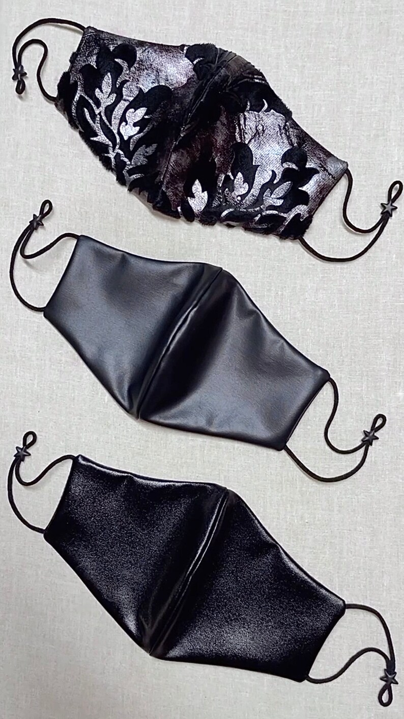 Puede incluir: Tres mascarillas, una con un patr&oacute;n floral negro y plateado y dos mascarillas de cuero negro.