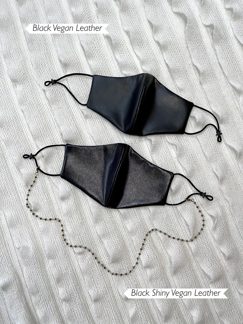 Puede incluir: Dos mascarillas negras con una cadena dorada. La mascarilla de arriba est&aacute; etiquetada como "Black Vegan Leather" y la de abajo como "Black Shiny Vegan Leather".