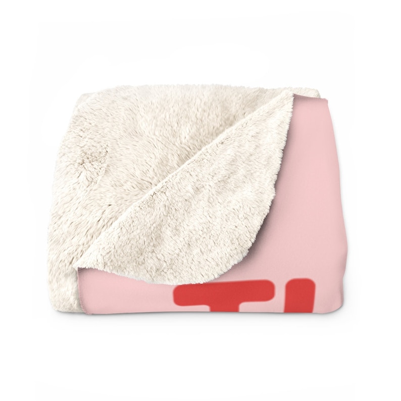 May include: A soft pink and white fleece throw blanket with a red "TI" design.