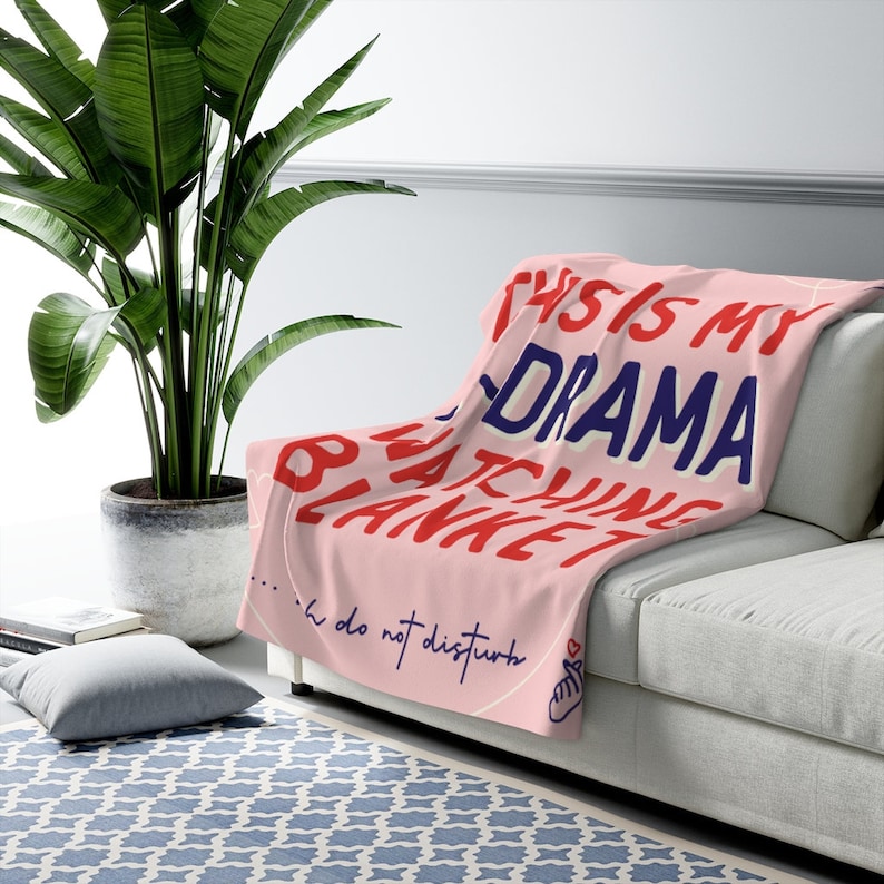 May include: Pink throw blanket with the text "This is my drama watching blanket...  do not disturb" in red, blue, and white lettering. A heart with a finger pointing to the left is at the bottom right corner.