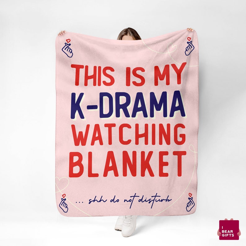 May include: Pink fleece blanket with the text "This is my K-Drama watching blanket... shh do not disturb" in red and blue lettering. The blanket has a pink heart with a finger heart gesture on each corner.