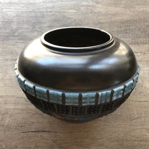 May include: A dark brown ceramic vase with a blue and black geometric design around the rim.