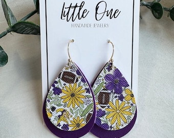 May include: Teardrop-shaped earrings with gold-colored hooks. The top layer features a floral and football design with yellow flowers and a football, while the bottom layer is solid purple. The earrings are displayed on a white card that reads "little One HANDMADE JEWELRY".