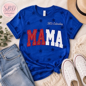May include: A royal blue short-sleeve t-shirt featuring a repeating star pattern and the word MAMA in large block letters. The letters MA are in red with a textured finish, while the letters MA are in white. The text SBD Embroidery is visible.