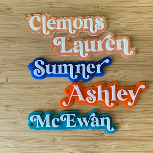 May include: Five acrylic name tags with white lettering on a wooden background. The names are Clemons, Laur&eacute;n, Summer, Ashley, and McEwan.