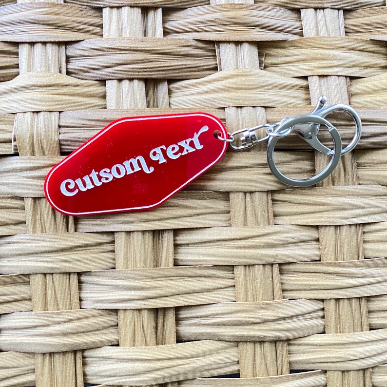 Op de afbeelding: Rode motel sleutelhanger met een zilveren sleutelring. De sleutelhanger heeft de tekst "Custom Text" in witte letters.