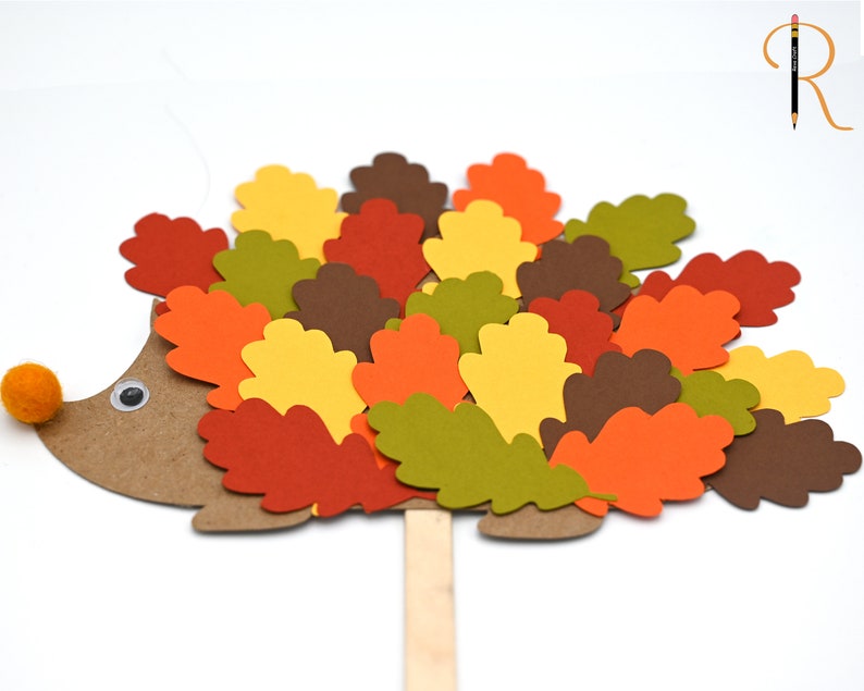 May include: A brown paper hedgehog with a googly eye and a red pom-pom nose. The hedgehog is covered in colorful paper leaves in shades of red, orange, yellow, green, and brown.