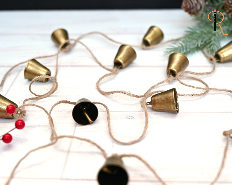May include: A string of small gold bells connected by twine. The bells are hanging on a white surface.