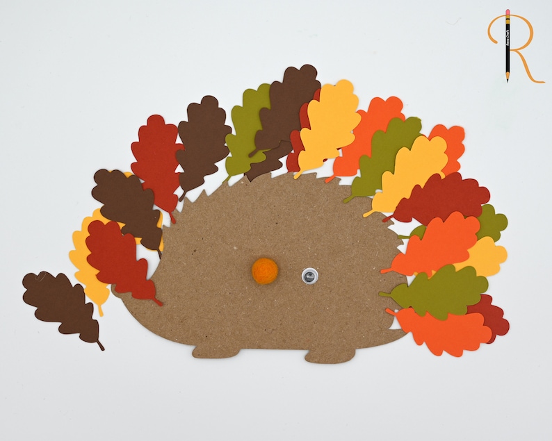 May include: A brown paper hedgehog with a googly eye and an orange pom-pom nose. The hedgehog is surrounded by fall-colored paper leaves in shades of red, orange, yellow, and green.