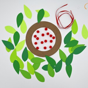 May include: A brown paper circle with red pom-poms on a white background surrounded by green and light green paper leaves. A red ribbon is also included.