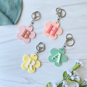 Peut inclure: Quatre porte-clés en forme de fleur avec des breloques en forme de lettres. Les porte-clés sont rose, vert, jaune et rose clair. Les lettres sont 'B', 'H', 'A' et 'R'.