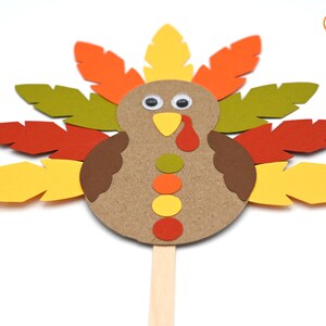 May include: A paper craft turkey with brown, orange, yellow, and green feathers. The turkey has a brown body with a yellow beak, red wattle, and googly eyes.