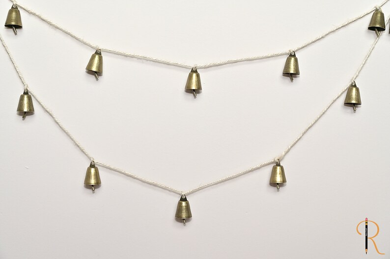 May include: A string of small, gold-colored bells hanging from a white string. The bells are evenly spaced and create a festive, whimsical look.