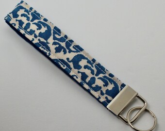 May include: A white and blue patterned fabric key chain with a silver metal key ring.
