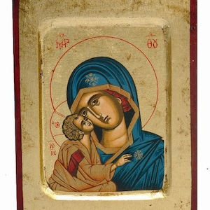 以下が含まれることがあります： 聖母マリアと幼子イエスを描いた、手描きの木製アイコン。アイコンは、赤い縁取りのある金色枠で囲まれています。聖母マリアは青いローブを着て、赤い頭巾をかぶっています。彼女は幼子イエスを腕に抱いています。幼子イエスは白いローブを着ています。アイコンは金色の後光で囲まれています。