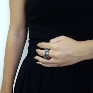 May include: A silver ring with multiple bands stacked on top of each other. The ring is worn on the middle finger of a person's hand.