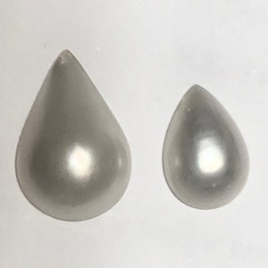 May include: Two pearlescent white teardrop-shaped beads, one larger than the other, on a white background.
