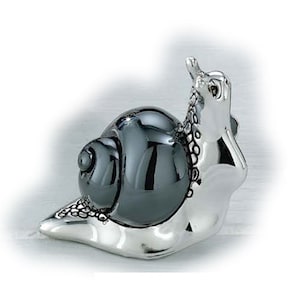May include: A decorative snail figurine with a shiny, dark gray shell and a silver-colored body. The snail's body is detailed with textured patterns, and it has a raised head and antennae.
