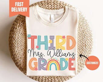 May include: A beige t-shirt with the text "THIRD" in colorful letters, followed by "Mrs. Williams" and "GRADE" in colorful letters with a rainbow graphic. The text "CUSTOMIZE!" is in a red circle.