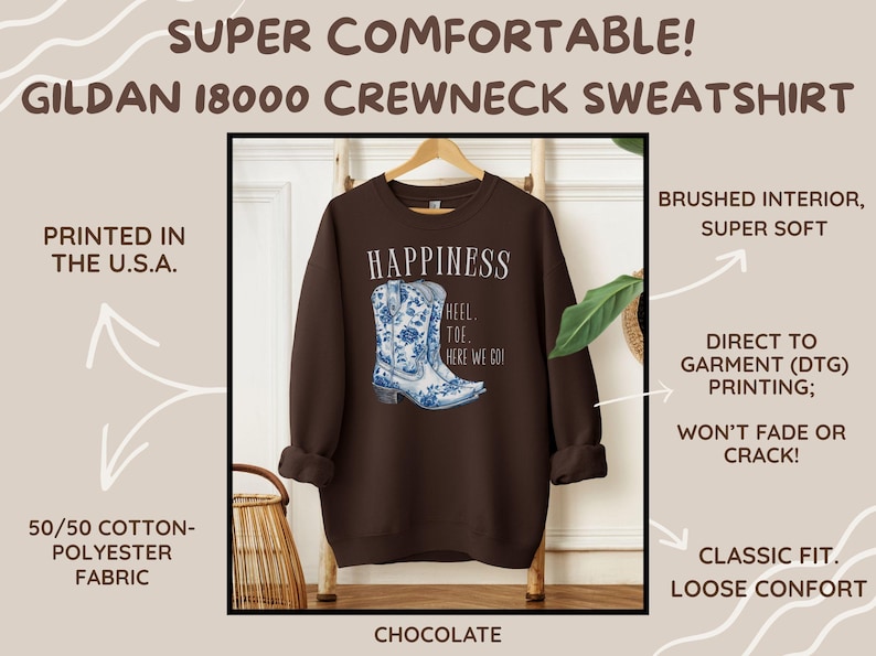 May include: A chocolate-coloured Gildan 18000 crewneck sweatshirt featuring a blue and white floral cowboy boot design. The word "HAPPINESS" is above the boot graphic, with "HEEL TOE HERE WE GO!" below. Made from a 50/50 cotton-polyester blend.