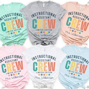 May include: A selection of t-shirts in shades like mint, grey, peach, pink, white, and pale blue. Each shirt displays the text "INSTRUCTIONAL ASSISTANT CREW LIMITED EDITION" in a retro style, with "Mrs. Wilkinson" printed beneath the design.