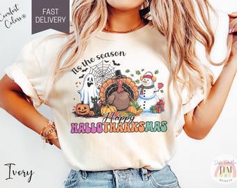 Könnte beinhalten: Ein weißes T-Shirt mit einem bunten Grafikdesign, das ein Gespenst, einen Truthahn und einen Schneemann zeigt. Der Text auf dem Shirt lautet "Tis the season Happy HalloThanksMas".