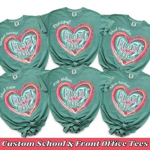 May include: Teal-colored t-shirts with a heart-shaped design that says "Front Office." Each shirt has a different title: Assistant Principal, Principal, School Counselor, School Nurse, Mrs. Wilson, and Admin Assistant. The text "Custom School & Front Office Tees" is at the bottom.