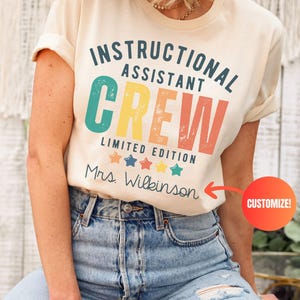 May include: A cream-coloured t-shirt featuring the text "INSTRUCTIONAL ASSISTANT CREW" in a retro font. Below the text are the words "LIMITED EDITION" and a row of stars. The name "Mrs. Wilkinson" is printed below the stars.