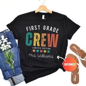 Może przedstawiać: Czarny T-shirt z napisem "First Grade Crew Limited Edition" w retro czcionce z kolorowymi akcentami. Pięć gwiazdek znajduje się pod tekstem, a napis "Mrs. Williams" znajduje się pod gwiazdkami. Napis "CUSTOMIZE!" znajduje się w czerwonym k&oacute;łku.