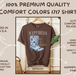 May include: Espresso-coloured t-shirt with a watercolour design of a blue and white cowboy boot. The shirt features the word "Happiness" and the phrase "Heel Toe Here We Go!" printed on the front. The shirt is made of garment-dyed, pre-shrunk cotton.