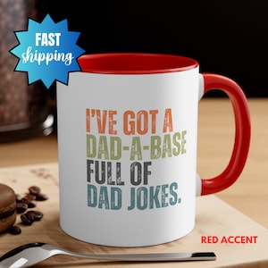 May include: White ceramic coffee mug with a red rim and handle. The mug has a vintage-style graphic that reads "I've got a dad-a-base full of dad jokes."