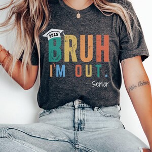 May include: Dark heather grey t-shirt with a rainbow graphic that says "BRUH I'M OUT. -Senior" and a graduation cap with the year 2025.
