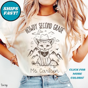 May include: Ivory-colored t-shirt with a graphic of a fox wearing a cowboy hat and a bandana that says "2nd Grade." The text "Howdy Second Grade" is above the fox, and "Ms. Carlson" is below. The shirt also has the text "Click for More Colors!"