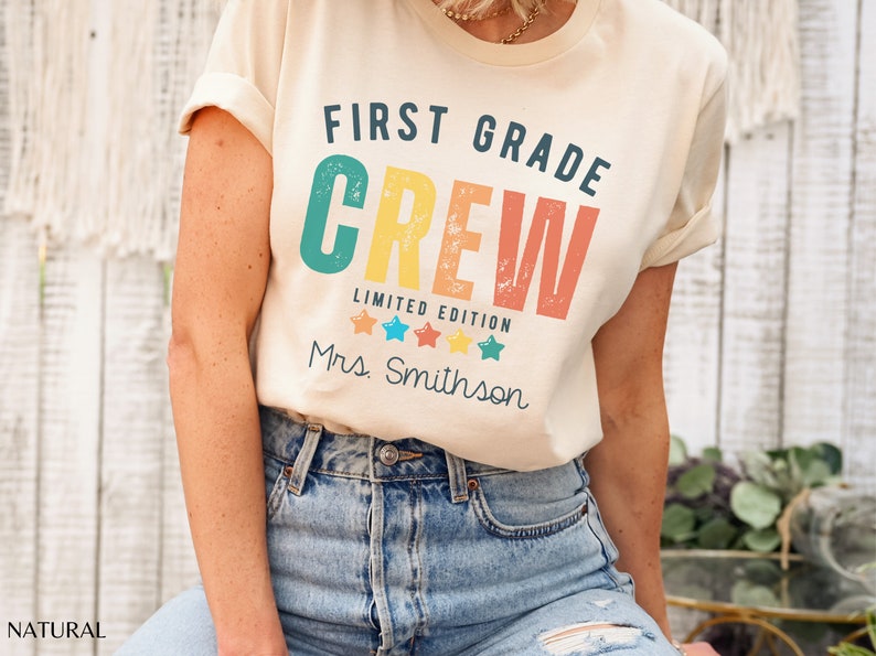 Może przedstawiać: Jasnobeżowa koszulka z napisem "First Grade Crew" w retro kolorystyce tęczy. Pod gł&oacute;wnym tekstem znajduje się napis "Limited Edition", a następnie cztery gwiazdki i napis "Mrs. Smithson".