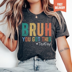 May include: A dark grey heather t-shirt with the text "BRUH YOU GOT THIS #TestDay!" in rainbow colors. The text is in a vintage style font.