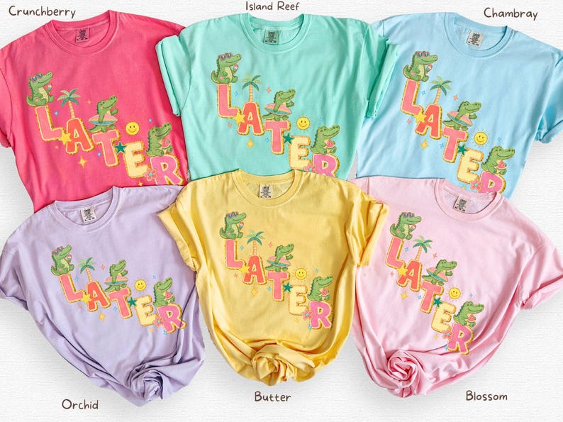 May include: A collection of colorful t-shirts in shades of pink, blue, green, yellow, and purple. Each shirt features a graphic design with the word "LATER" and cartoon alligators, palm trees, and a smiley face. The shirts are casual wear.