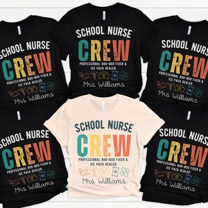 May include: A collection of black and cream-colored t-shirts with the text "SCHOOL NURSE CREW" in a colorful, vintage-style design. The shirts also include the text "PROFESSIONAL 800-800 FIXER & ICE PACK DEALER" and "Mrs. Williams".