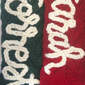 Peut inclure: Deux chaussettes de No&euml;l en tricot avec des lettres en fil blanc. La chaussette de gauche est verte avec le mot "Happy" brod&eacute; dessus. La chaussette de droite est rouge avec le mot "Merry" brod&eacute; dessus.