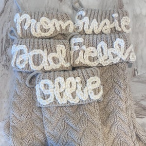 Peut inclure: Ensemble de quatre chaussettes en tricot beige avec des noms brod&eacute;s en blanc&nbsp;: Maman, Gracie, Papa et Ellie.