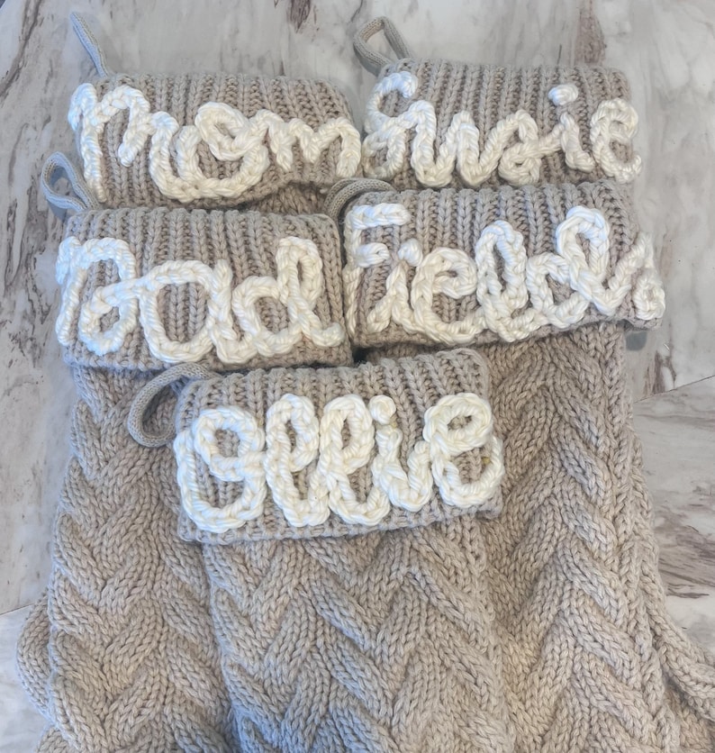 Peut inclure: Ensemble de quatre chaussettes en tricot beige avec des noms brod&eacute;s en blanc&nbsp;: Maman, Gracie, Papa et Ellie.